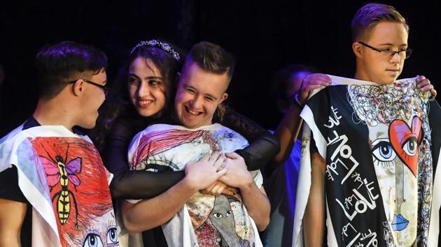 A child gets a hug while presenting ponchos during the “heART Couture” show. During the fashion show, most children showed portraits of wide-eyed characters, and messages written in English focused on love and family. Some has their images produced by a professional designer who created images interpreting the kids’ suggestions. (Andreea Alexandru/AP) A child gets a hug while presenting ponchos during the “heART Couture” show. During the fashion show, most children showed portraits of wide-eyed characters, and messages written in English focused on love and family. Some has their images produced by a professional designer who created images interpreting the kids’ suggestions. (Andreea Alexandru/AP)