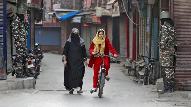 A Kashmir girl rides her bike past security force personnel standing guard in front closed shops in a street in Srinagar. (REUTERS) A Kashmir girl rides her bike past security force personnel standing guard in front closed shops in a street in Srinagar. (REUTERS)