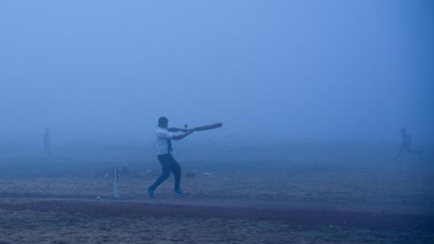 A man plays a shot during a street cricket match even as dense fog enveloped parts of Pune. (Sanket Wankhade/HT Photo)