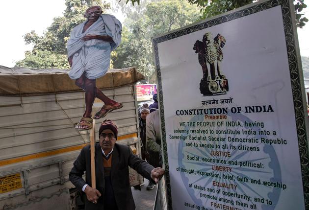 The massive protests against the CAA have brought the Constitution into the public discourse. A demonstrator stands next to a hoarding of the Preamble to the Constitution in Delhi.(REUTERS)