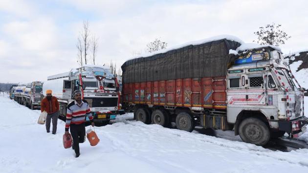 Men carry containers as trucks are seen stranded in the snow at Srinagar Jammu national highway. Stranded truck drivers said they have run out of money to buy food and urged the government to come to their aid. They said the government has not made any arrangement for setting up community kitchens for them. (Waseem Andrabi / HT Photo)