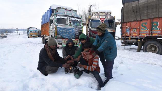 Men warm themselves around a fire with trucks stranded in the snow. Meanwhile, Hindustan Construction Company (HCC) was able to clear the debris from the landslides in Digdole area to make way for one-way traffic. At around 4.30pm, traffic police gave a go ahead to the 200 Jammu-bound trucks, stranded since Sunday in the Ramban area. (Waseem Andrabi / HT Photo)