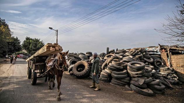 A labourer stands before piles of stacked tyres as a horse-drawn cart carrying wooden beams passes by. “It requires physical strength to carry around the heavy tyres,” he said to AFP. “If we had the option of a more stable occupation, we would have quit this one. But this is our only source of income.” (Khaled Desouki / AFP) A labourer stands before piles of stacked tyres as a horse-drawn cart carrying wooden beams passes by. “It requires physical strength to carry around the heavy tyres,” he said to AFP. “If we had the option of a more stable occupation, we would have quit this one. But this is our only source of income.” (Khaled Desouki / AFP)