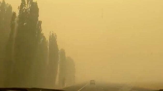 A vehicle is engulfed in yellowish smoke as it travels along a highway during bushfires near New South Wales, Australia.(Reuters)