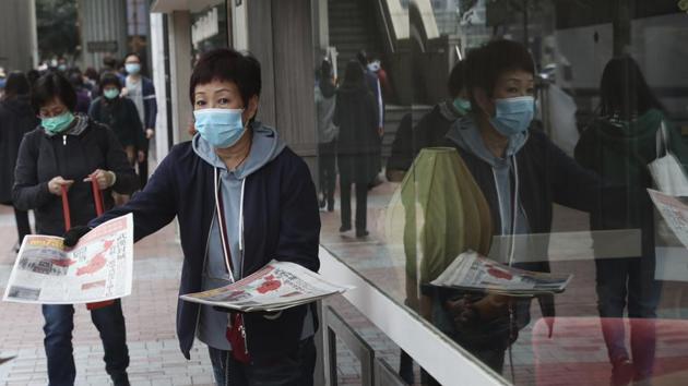 A woman wearing a protective face mask delivers a leaflet on coronavirus in Wuhan, in Hong Kong on Friday. China broadened its unprecedented, open-ended lockdowns to encompass around 25 million people to try to contain a new virus that has sickened hundreds.(AP Photo)