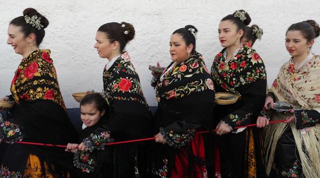 Women parade in colorful embroidered shawls and skirts as music plays. A priest also attends. (Manu Fernandez / AP)