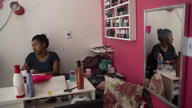In Rio’s North Zone, the Arara Park favela is so packed that a string of one-room shops were built over an open sewage canal. Ingrid Rocha, 20, slouches beneath a whirring ceiling fan with another on the floor. Her air conditioning unit does nothing to cut the heat, so clients only show up after 4pm. That means Rocha, who’s pregnant, needs to work more than 12-hour days to hit her targets. (Silvia Izquierdo / AP) In Rio’s North Zone, the Arara Park favela is so packed that a string of one-room shops were built over an open sewage canal. Ingrid Rocha, 20, slouches beneath a whirring ceiling fan with another on the floor. Her air conditioning unit does nothing to cut the heat, so clients only show up after 4pm. That means Rocha, who’s pregnant, needs to work more than 12-hour days to hit her targets. (Silvia Izquierdo / AP)