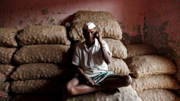 A labourer talks on his mobile phone as he sits on sacks of onions at a wholesale market in Mumbai.(Photo: Reuters)