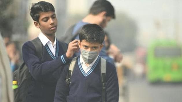 A student helps another with an anti pollution facemask on their way to school, in New Delhi.(Raj K Raj/HT File)
