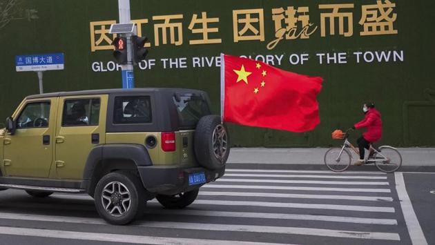 A vehicle flying a Chinese flag drives past a woman wearing a face mask as she rides a bicycle along a street in Wuhan. “We met in the middle. We need to be cautious but we will not panic,” Jenina said. They recounted their survival and escape from Wuhan to The Associated Press via Skype from their new room in a military hospital in Poland where they are under a 14-day quarantine. (Arek Rataj / AP)