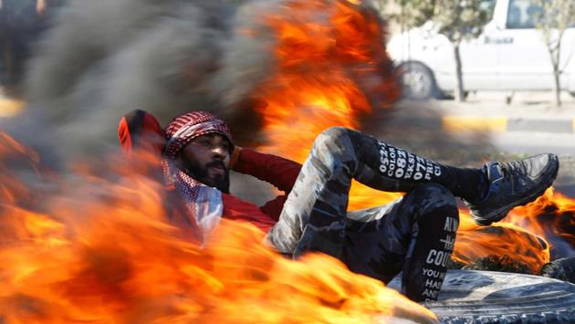 An Iraqi demonstrator sits amid burning tires blocking a road during ongoing anti-government protests in Najaf, Iraq. (Alaa al-Marjani / REUTERS)