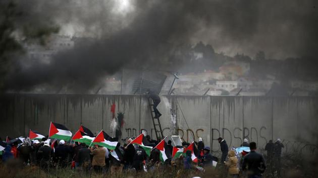 A Palestinian protester escalates Israel’s controversial security wall as others waving national flags burn tyres during a demonstration against a US-brokered peace proposal, in the occupied West Bank village of Bilin near Ramallah. (Abbas Momani / AFP)