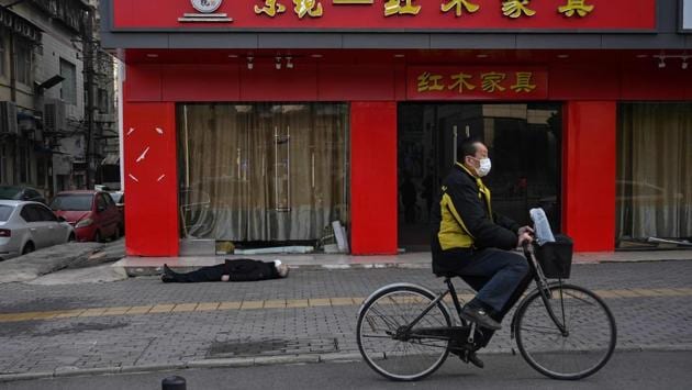 A man wearing a facemask cycles past an elderly man who collapsed and died on the pavement along a street near a hospital in Wuhan, on January 30. The body of this man in his 60s lay stiff on his back in front of a closed furniture store, near the hospital. He was still wearing a facemask. Officials in hazard suits took every precaution as they approached the body. (Hector Retamal / AFP)