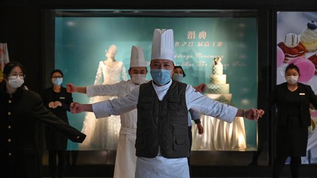 Hotel workers sport protective face masks as they exercise in the lobby during a staff briefing about how to implement new regulations concerning the current situation in Wuhan in China’s central Hubei province, on January 28. In hospitals, people queued up in long lines to see a doctor. The wait was so long that some had brought their own chairs. (Hector Retamal / AFP)