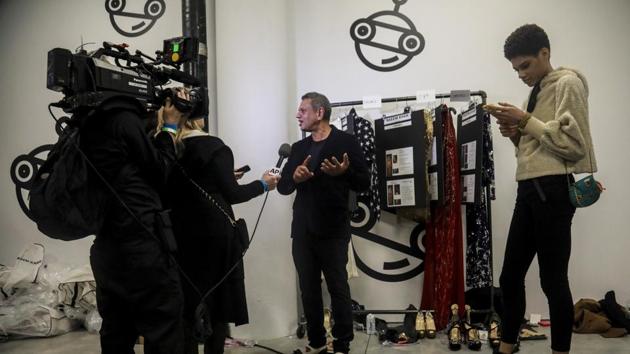 A model waits to the side, right, while fashion designer Naeem Khan, center, gives a backstage interview before unveiling his latest creations. (AP)