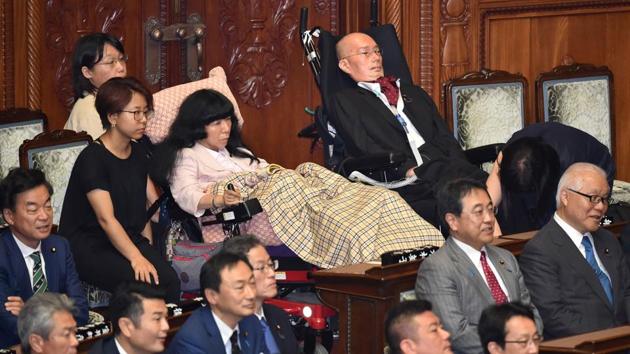 Fellow lawmaker Yasuhiko Funago (top, R) has amyotrophic lateral sclerosis (ALS), meaning he cannot speak, and communicates by blinking to his carer or operating a computer system with his mouth. But he is demanding to be heard in the fight to improve the lives of people with disabilities in Japan. (Kazuhiro Nogi / AFP)