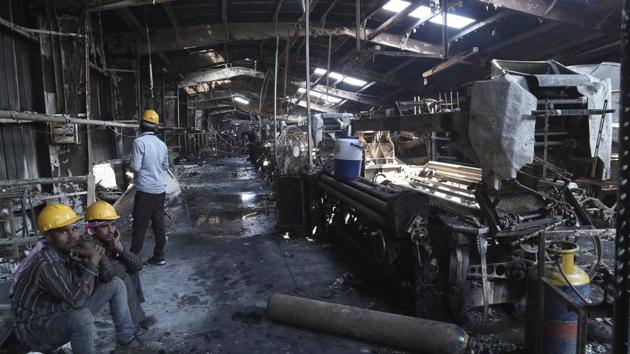 Labourers sit near burnt remains in the factory.Surviving workers, who are paid about Rs25 per hour, said conditions had been dangerous. “We work almost 14 hours a day. But do we have an option?” said Vimalbhai, a textile worker, who goes by only one name. “Every once a while there is a fire in some factory or the other. Nobody cares and we keep on working.” (AP Photo)