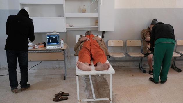A foreign prisoner on examining table next to a doctor in a prison in Hasaka. In a hospital on the ground floor, about 100 men crowded on to around half the number of beds suffering from ailments and injuries. Several were in orange jumpsuits, similar to those often worn by IS captives before they were executed. (Goran Tomasevic / REUTERS)