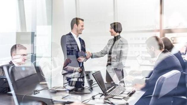 Sealing a deal. Business people shaking hands, finishing up meeting in corporate office. Businessmen working on laptop seen in glass reflection. Business and entrepreneurship concept.(Getty Images/iStockphoto)