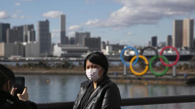 In this file photo, a tourist wearing a mask poses for a photo with the Olympic rings in the background, at Tokyo's Odaiba district.(AP) In this file photo, a tourist wearing a mask poses for a photo with the Olympic rings in the background, at Tokyo's Odaiba district.(AP)