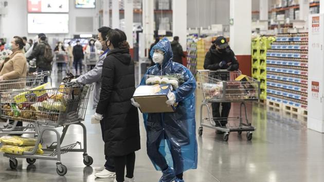 A woman wearing a protective mask and poncho carries a bundle of fruit and vegetables towards the checkout area at a supermarket in Shanghai, China. (Bloomberg)