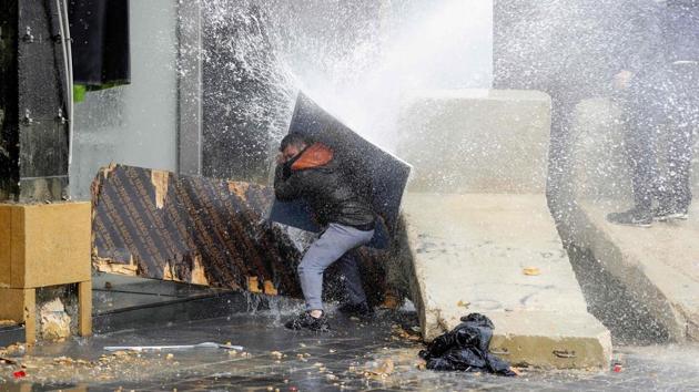 An anti-government protester uses a piece of wood to block a water cannon in central Beirut, Lebanon, during protests on February to stop a confidence vote for a new government, which they say fails to address their demands and cannot rescue the ailing country. (Joseph Eid / AFP)