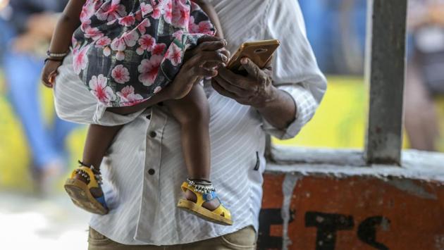 A man uses a smartphone while carrying a child in Mumbai. In India, where the internet—and fake news—are still relatively new phenomenon, a false report of rampant child abduction and organ harvesting circulated widely via WhatsApp, leading to mob violence and over three dozen fatal lynchings in 2017 and 2018. (Dhiraj Singh / Bloomberg)