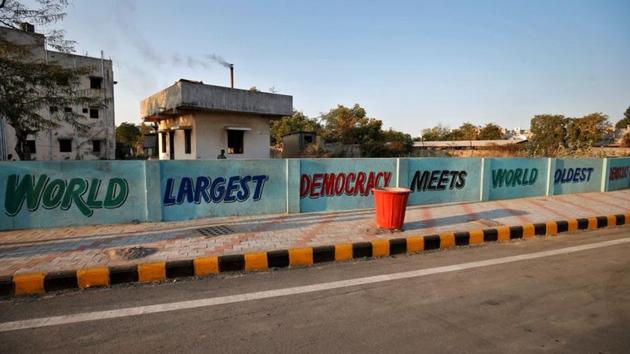 A boy looks from behind a wall painted with a message, along the route that US President Trump and PM Modi will be taking on February 24. More than 50,000 people are expected to line up along the 22km route of the roadshow. (Amit Dave / REUTERS)