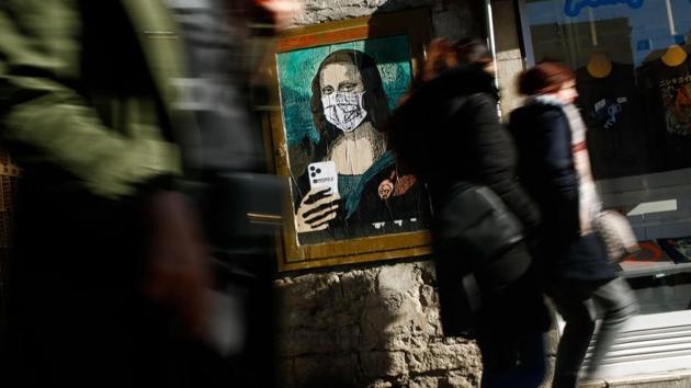 People walk by a poster by Italian urban artist Salvatore Benintende aka “TVBOY” depicting Leonardo da Vinci's Mona Lisa wearing a facemask and holding a mobile phone reading “Mobile World Virus” in Barcelona, Spain, a week after the World Mobile Congress was cancelled due to fears stemming from the coronavirus that sparked an exodus of industry heavyweights. (Pau Barrena / AFP)