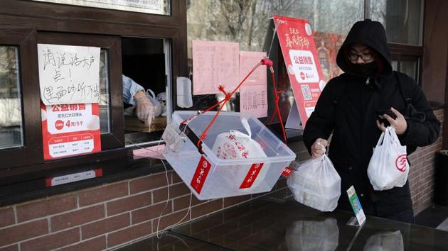 A man collects bags of his food order as a worker passes in a basket customers to prevent human contact. Yunhaiyao remains worried about expenses and has taken a 10 million yuan loan to ease cash-flow pressures. One way out is to “share” employees with other businesses that are enjoying an increase in demand: e-commerce platforms. (Andy Wong / AP)
