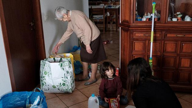 Ines Prandini, 85, takes food from a shopping bag full of food supplies, as her two-year-old granddaughter Bianca Toniolo sits with her mother Chiara Zuddas at home in San Fiorano. (Marzio Toniolo / REUTERS)