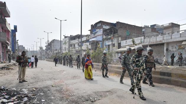 A woman walks along security personnel patrolling a street, at Khajuri Khas area of northeast Delhi on Friday.(PTI Photo) A woman walks along security personnel patrolling a street, at Khajuri Khas area of northeast Delhi on Friday.(PTI Photo)