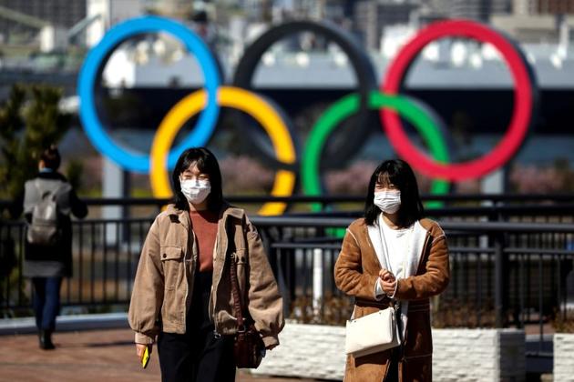 People wearing protective face masks, following an outbreak of the coronavirus, are seen in front of the Giant Olympic rings at the waterfront area at Odaiba Marine Park in Tokyo, Japan. Seventy cases — the largest from a single prefecture in Japan — have been detected in the northernmost main island of Hokkaido, where experts have raised concern about growing clusters of patients with unknown transmission routes. (Athit Perawongmetha / REUTERS)