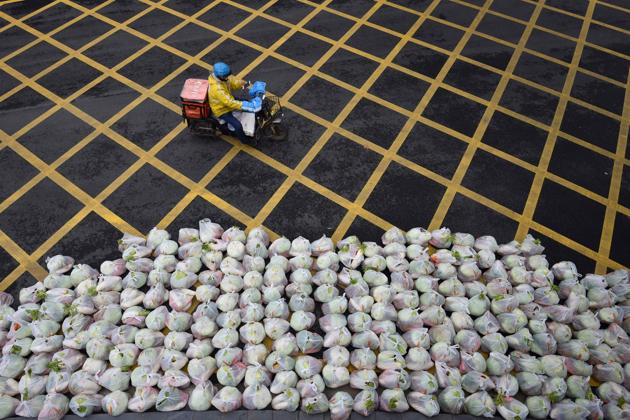 A man rides past bags of vegetables being prepared for delivery on an almost empty street in Wuhan, in China's central Hubei province. A viral outbreak that began in China has infected more than 85,000 people globally. The World Health Organisation has named the illness COVID-19, referring to its origin late last year and the coronavirus that causes it. (AFP)