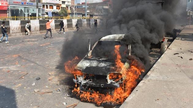 A car is set on fire as protesters rage ahead in the background at Bhajanpura on February 24. (Sanchit Khanna / HT Photo)