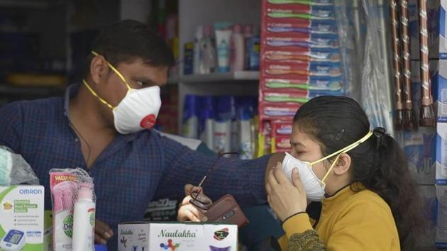 A salesman at a chemist’s shop helps a buyer to wear her protective mask.(PTI PHOTO.)