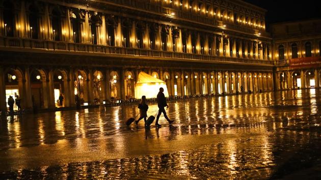 Tourists pull their luggage as they walk through a nearly empty St. Mark's Square on a rainy day in Venice, Italy. The coronavirus outbreak in northern Italy has so overwhelmed the public health system that officials are taking extraordinary measures to care for the sick, seeking to bring doctors out of retirement and accelerate graduation dates for nursing students. (Francisco Seco / AP) Tourists pull their luggage as they walk through a nearly empty St. Mark's Square on a rainy day in Venice, Italy. The coronavirus outbreak in northern Italy has so overwhelmed the public health system that officials are taking extraordinary measures to care for the sick, seeking to bring doctors out of retirement and accelerate graduation dates for nursing students. (Francisco Seco / AP)