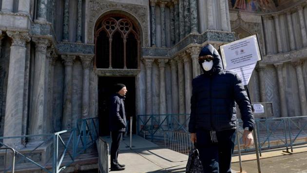 A tourist wearing a protective face mask leaves the basilica of San Marco in Venice. The economic losses are piling up in a city already going under, given the more existential, long-term threat that Venice is sinking. (Andrea Pattaro / AFP) A tourist wearing a protective face mask leaves the basilica of San Marco in Venice. The economic losses are piling up in a city already going under, given the more existential, long-term threat that Venice is sinking. (Andrea Pattaro / AFP)