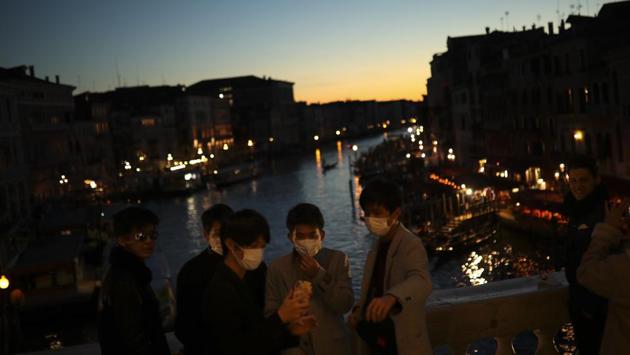 Tourists wearing protective masks pose for a photograph at the Rialto bridge as the sun sets in Venice. Venice has remained quiet ever since the first coronavirus casualty. Only residents and intrepid tourists wearing a different type of mask — surgical ones — remain to take advantage of a hauntingly beautiful jewel of a city that otherwise would be jammed. (Francisco Seco / AP) Tourists wearing protective masks pose for a photograph at the Rialto bridge as the sun sets in Venice. Venice has remained quiet ever since the first coronavirus casualty. Only residents and intrepid tourists wearing a different type of mask — surgical ones — remain to take advantage of a hauntingly beautiful jewel of a city that otherwise would be jammed. (Francisco Seco / AP)