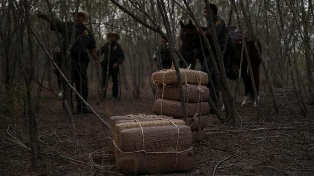 Border patrol agents surround what they said was about 140 pounds of marijuana which was abandoned by smugglers in La Joya. Many smugglers are linked to drug trafficking gangs. In April, border agents hear about a group who they believe are bringing in marijuana. They chase them in the dark and catch about 30 men on a river bank studded with spiky cactus plants -- reported Reuters. (Adrees Latif / REUTERS)