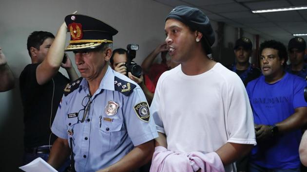 Former soccer star Ronaldinho talks as he walks escorted by Police officers with hands handcuffed to declare to judge Clara Ruiz Diaz at Justice Palace in Asuncion, Paraguay, Saturday, March 7, 2020. Ronaldinho and his brother Roberto de Assis Moreira, right back, were alleged to enter to the country with a false Paraguayan passport.(AP Photo/Jorge Saenz)(AP) Former soccer star Ronaldinho talks as he walks escorted by Police officers with hands handcuffed to declare to judge Clara Ruiz Diaz at Justice Palace in Asuncion, Paraguay, Saturday, March 7, 2020. Ronaldinho and his brother Roberto de Assis Moreira, right back, were alleged to enter to the country with a false Paraguayan passport.(AP Photo/Jorge Saenz)(AP)