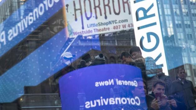 Tourists wear face masks as news about the coronavirus is seen in a reflection off a glass surface in Times Square in New York. President Donald Trump on Sunday called on Americans to cease hoarding groceries and other supplies, while one of the nation's most senior public health officials called on the nation to act with more urgency to safeguard their health. (Wong Maye-E / AP) Tourists wear face masks as news about the coronavirus is seen in a reflection off a glass surface in Times Square in New York. President Donald Trump on Sunday called on Americans to cease hoarding groceries and other supplies, while one of the nation's most senior public health officials called on the nation to act with more urgency to safeguard their health. (Wong Maye-E / AP)
