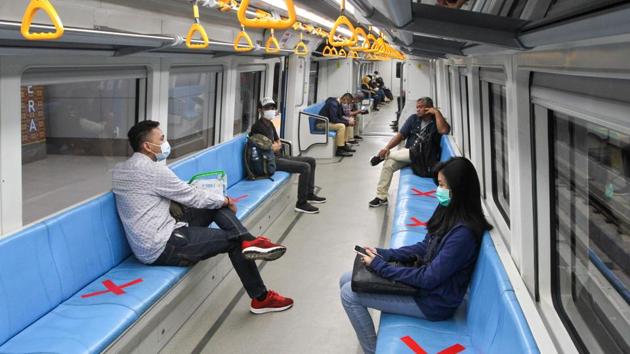 People sit on designated areas decided by red cross marks to ensure social distancing inside a light rapid transit train in Palembang, South Sumatra amid COVID-19 outbreak. (Abdul Qodir / AFP)