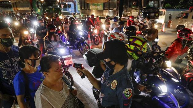 A police officer reads the temperatures of people at a checkpoint as part of precautionary measures against the spread of the new coronavirus in Manila, Philippines.(AP)