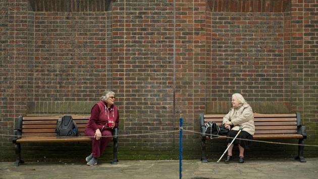 Two women observe social distancing measures as they speak to each other from adjacent park benches amid the novel coronavirus COVID-19 pandemic, in the centre of York, northern England. (Oli Scarff / AFP)