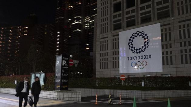 Two men walk past a large banner promoting the Tokyo 2020 Olympics in Tokyo. (AP) Two men walk past a large banner promoting the Tokyo 2020 Olympics in Tokyo. (AP)