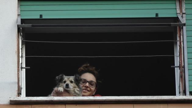 A girl and her dog look out from a window during one of the many flash mobs taking place these days in Rome, Sunday, March 15, 2020. The nationwide lockdown to slow coronavirus is still early days for much of Italy, but Italians are already showing signs of solidarity with flash mob calls circulating on social media for people to ''gather'' on their balconies at certain hours, either to play music or to give each other a round of applause. For most people, the new coronavirus causes only mild or moderate symptoms. For some, it can cause more severe illness, especially in older adults and people with existing health problems. (AP Photo/Alessandra Tarantino)(AP) A girl and her dog look out from a window during one of the many flash mobs taking place these days in Rome, Sunday, March 15, 2020. The nationwide lockdown to slow coronavirus is still early days for much of Italy, but Italians are already showing signs of solidarity with flash mob calls circulating on social media for people to ''gather'' on their balconies at certain hours, either to play music or to give each other a round of applause. For most people, the new coronavirus causes only mild or moderate symptoms. For some, it can cause more severe illness, especially in older adults and people with existing health problems. (AP Photo/Alessandra Tarantino)(AP)