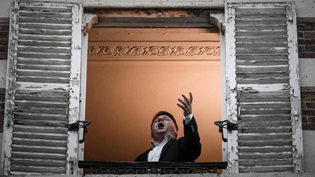 French opera tenor singer Stephane Senechal performs the song O sole mio from his window in Paris on March 26, 2020 on the evening of the tenth day of a strict lockdown in France aimed at curbing the spread of COVID-19.(AFP)