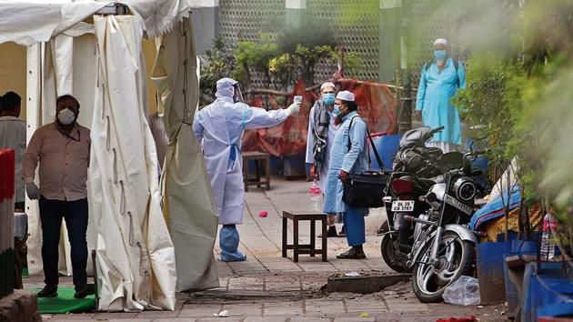 A volunteer wearing protective suit checks temperature of a man at Nizamuddin during coronavirus lockdown, in New Delhi.(ANI Photo/Prabhat Mehrotra)