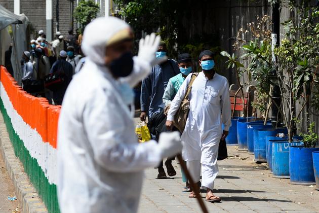 A policeman (L) gestures as men wearing protective facemasks walk to board a special service bus taking them to a quarantine facility amid concerns about the spread of the COVID-19 coronavirus in Nizamuddin area of New Delhi on March 31, 2020.(AFP)